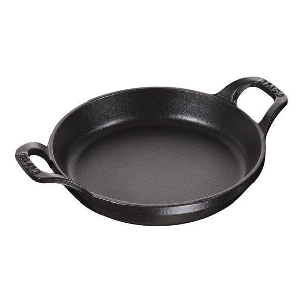 A black Staub round gratin pan with two handles.