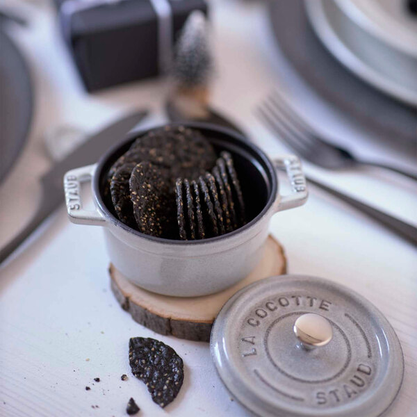 A white Staub mini Dutch oven filled with cookies on a table.