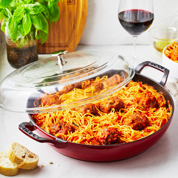 A Staub enameled cast iron brazier with a glass lid filled with spaghetti and meatballs.
