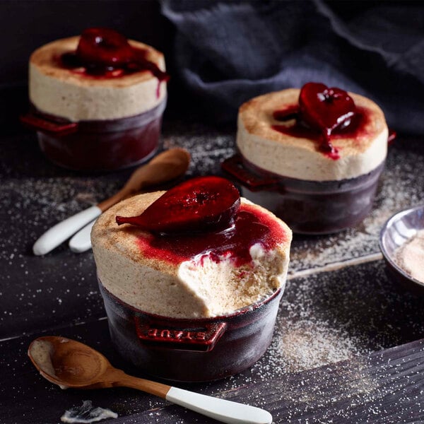A Staub Grenadine enameled cast iron mini Dutch oven with three desserts topped with fruit and whipped cream.