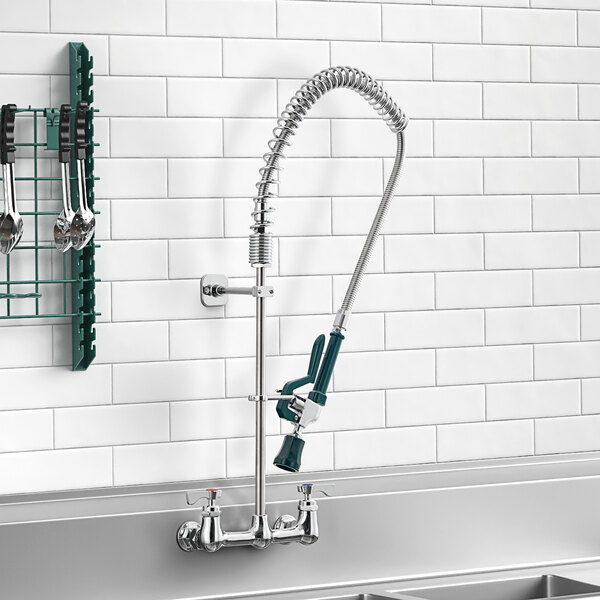 A Krowne wall-mount pre-rinse faucet above a sink with utensils.