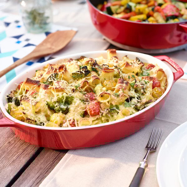 A red Staub casserole dish with pasta and broccoli on a table.