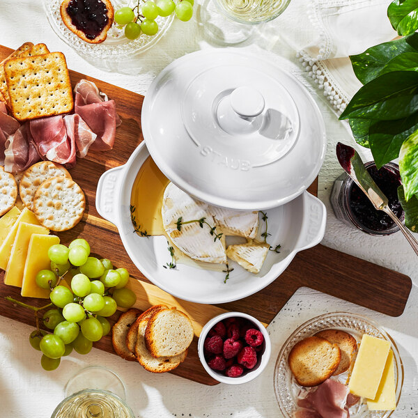 A table with a white ceramic pot with a lid of food and fruit.