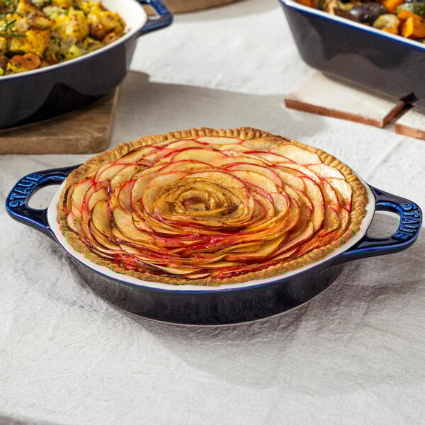 A pie in a Staub round dark blue ceramic pie dish on a table.