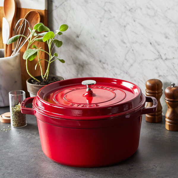 A Staub cherry red enameled cast iron Dutch oven with a lid on a counter.