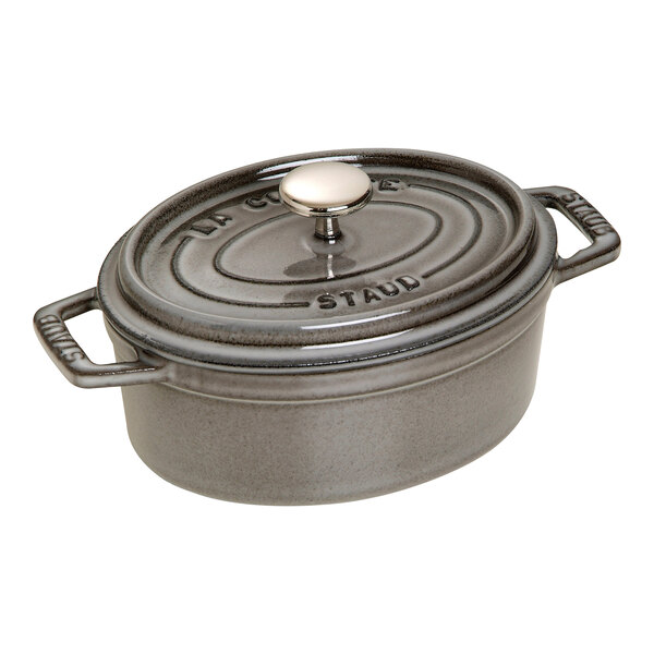 A graphite gray Staub enameled cast iron oval Dutch oven with a lid and handle.