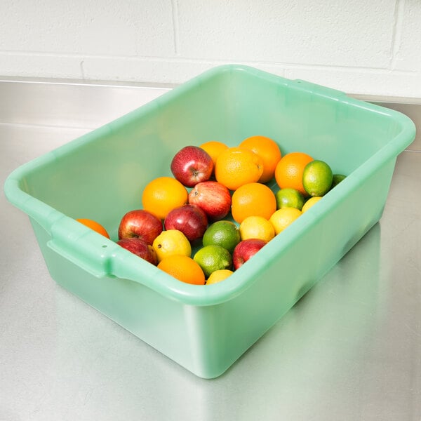 A Vollrath Traex green food storage box filled with fruit including oranges, a lemon, and a red apple.