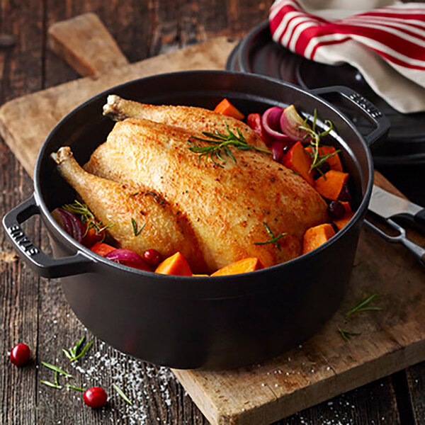 A Staub black enameled cast iron Dutch oven with chicken and vegetables cooking inside.