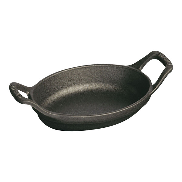 A black Staub enameled cast iron oval gratin pan with two handles.