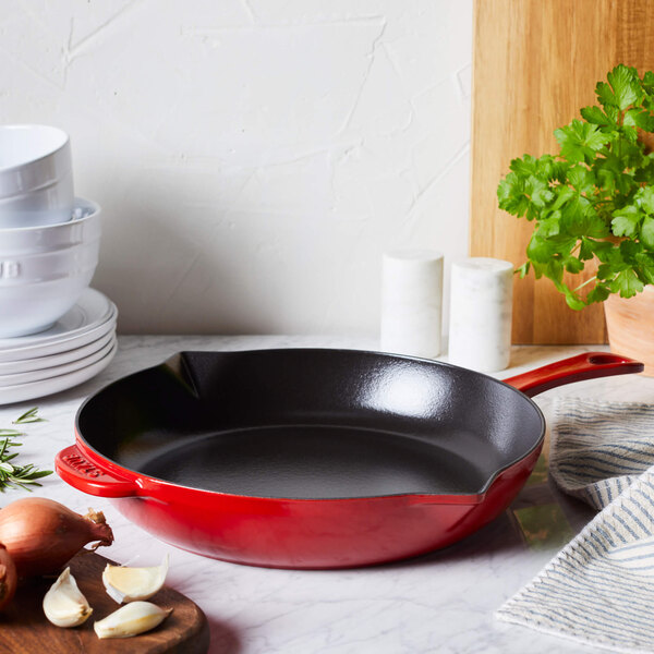 A red Staub enameled cast iron skillet on a counter.