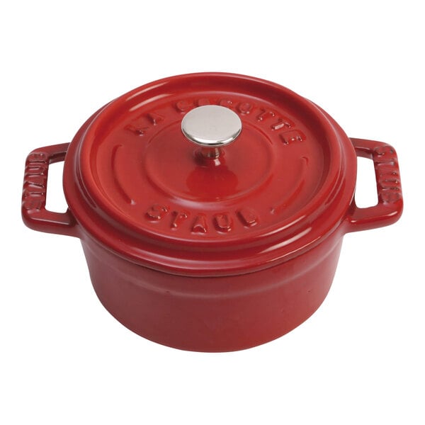 A Staub cherry red enameled cast iron mini Dutch oven with a lid and handle.