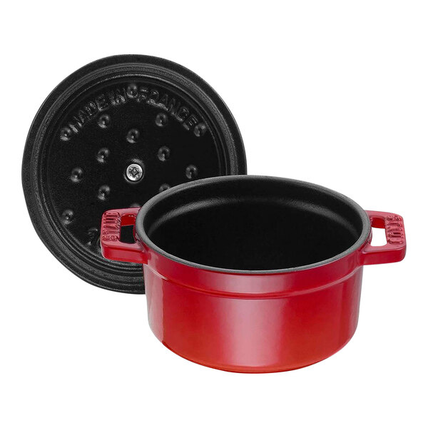 A close-up of a red Staub enameled cast iron pot with a black lid.