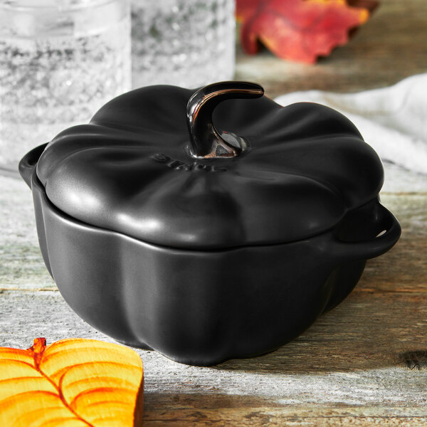 A black ceramic Staub pumpkin mini Dutch oven with a handle.