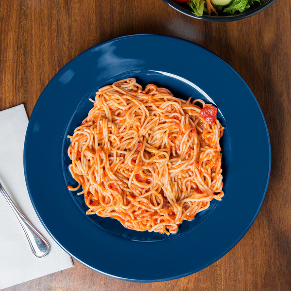 A plate of spaghetti with sauce on it and a bowl of salad on a table.