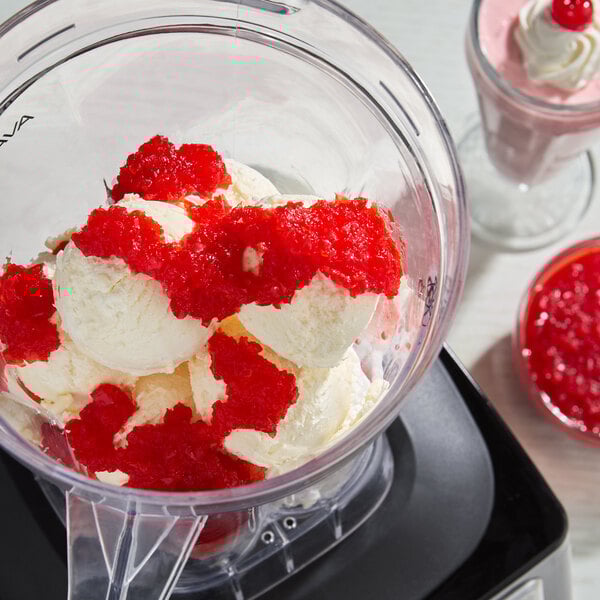 A blender container filled with scoops of vanilla ice cream topped with crushed maraschino cherries.