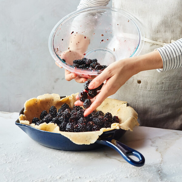 A hand reaching for blackberries in a Staub dark blue enameled cast iron skillet.
