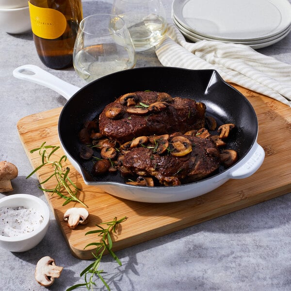 A Staub enameled cast iron skillet with meat and mushrooms cooking in it.