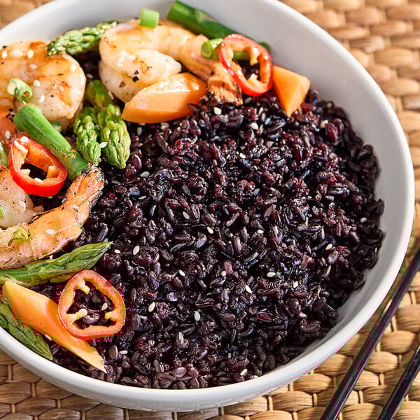 A bowl of black rice with shrimp, tomato, and asparagus.