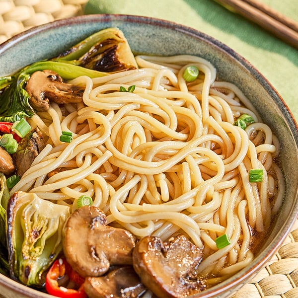 A bowl of Lotus Foods brown udon rice noodles with mushrooms and vegetables.