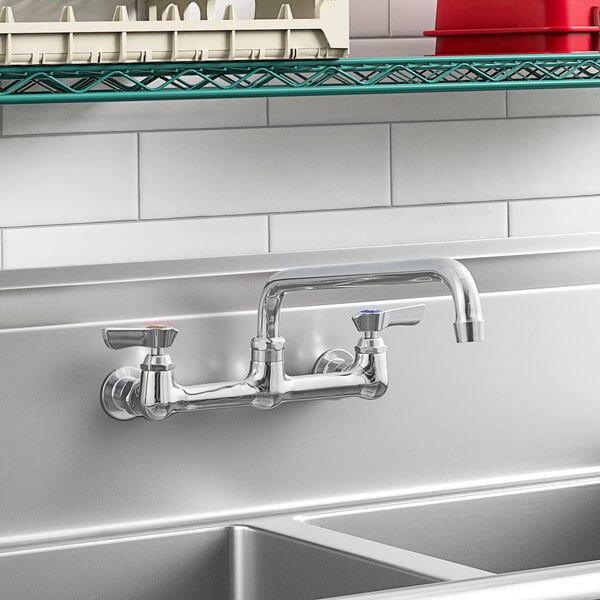 A Krowne wall-mount faucet with lever handles and a swing nozzle above a stainless steel sink.