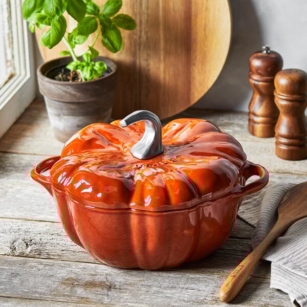 A Staub burnt orange pumpkin enameled cast iron Dutch oven on a table.