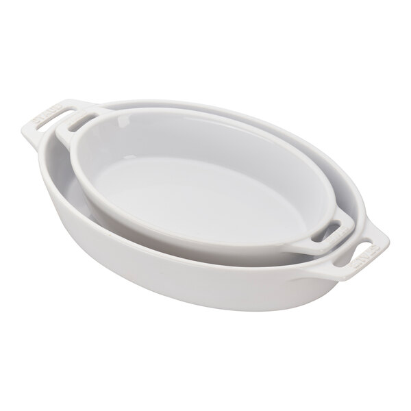A white Staub oval baking dish set with handles.