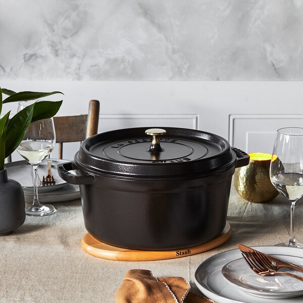 A black Staub enameled cast iron pot with a lid on a table with a fork and a plate.