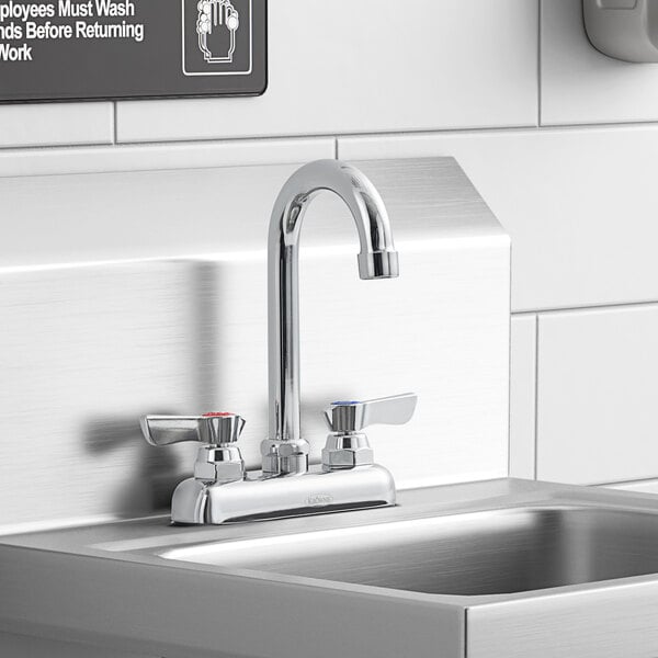 A Krowne deck-mount faucet with lever handles and a gooseneck nozzle installed on a counter above a stainless steel sink.