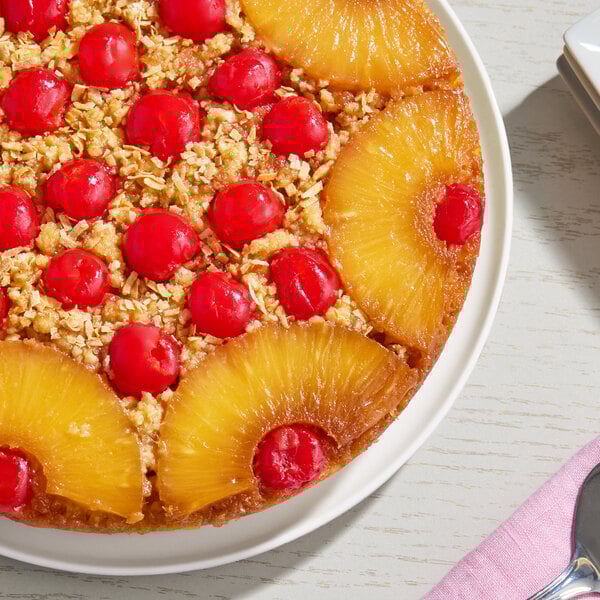 A pineapple upside-down cake topped with maraschino cherries and pineapple rings on a white plate.