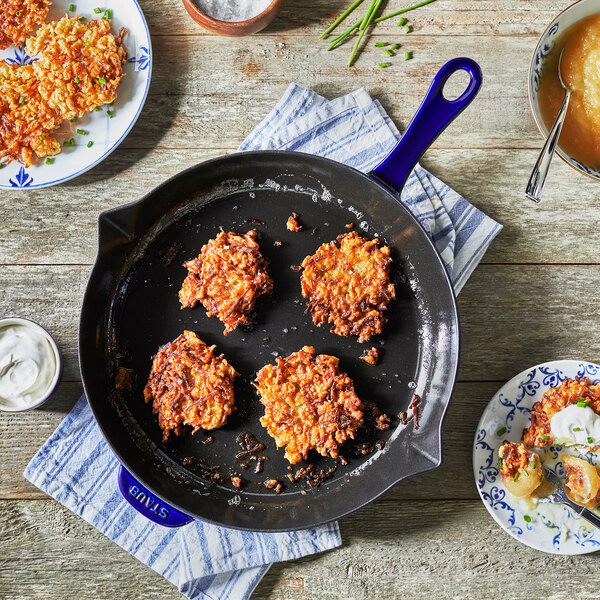 A Staub dark blue enameled cast iron skillet with food in it on a table.