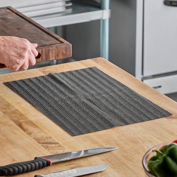 A black non-slip plastic cutting board liner placed on a wooden countertop.