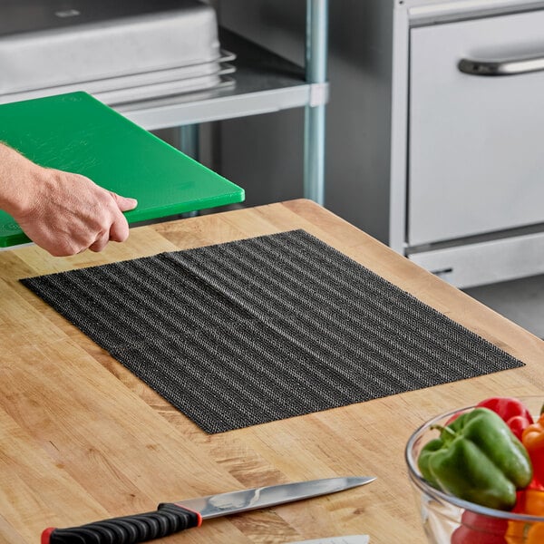 A black non-slip plastic cutting board liner placed on a wooden countertop.