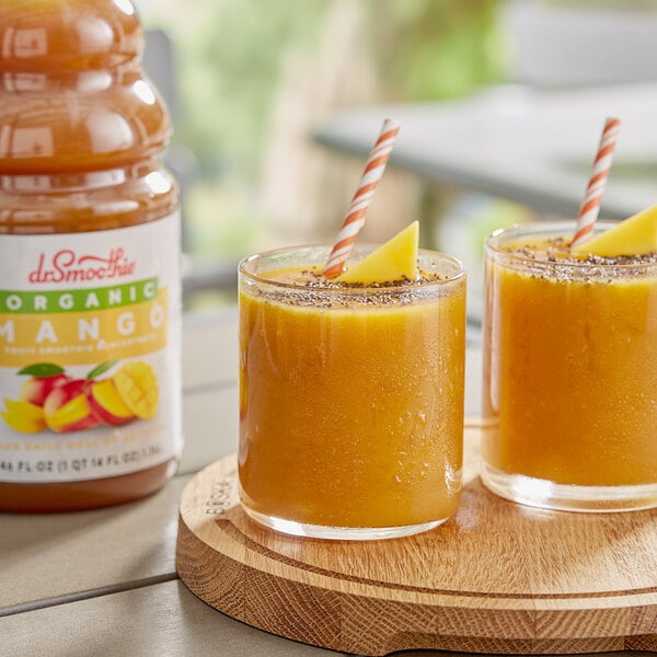 Two glasses of mango smoothie with straws on a table.
