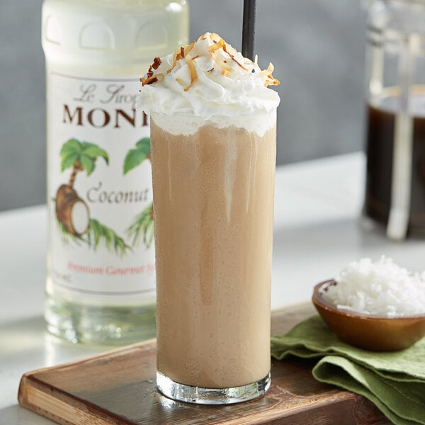 A glass of brown liquid with whipped cream and coconut flakes with a straw in it.