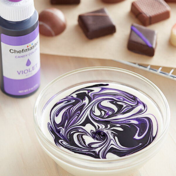 A bowl of white and purple liquid with a Chefmaster Violet Oil-Based Candy Color bottle in the background.