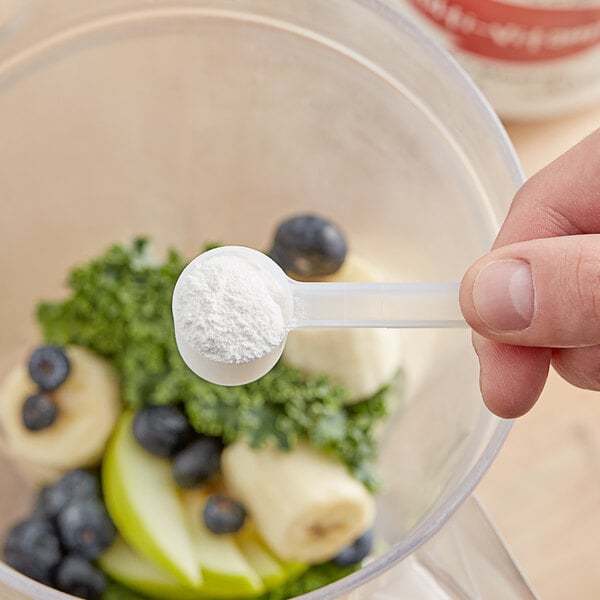 A hand holding a spoon with white powder on it over a bowl of fruit.