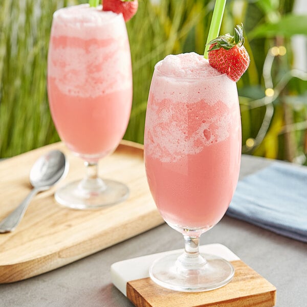 Two glasses of pink Fanale strawberry drinks with straws and a strawberry on top.