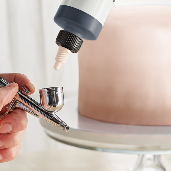 A person using a silver airbrush to spray color onto a cake.