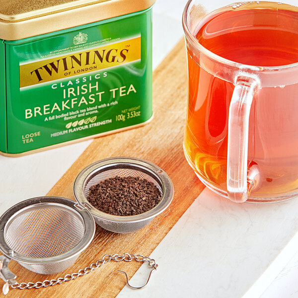 A tea cup and a strainer next to a box of Twinings Irish Breakfast Loose Leaf Tea.