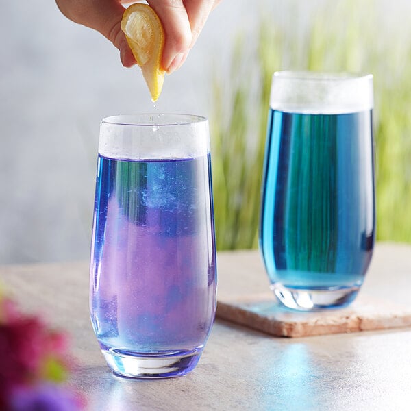 A hand squeezing a lemon into a glass of blue Wild Hibiscus Butterfly Pea Flower tea.