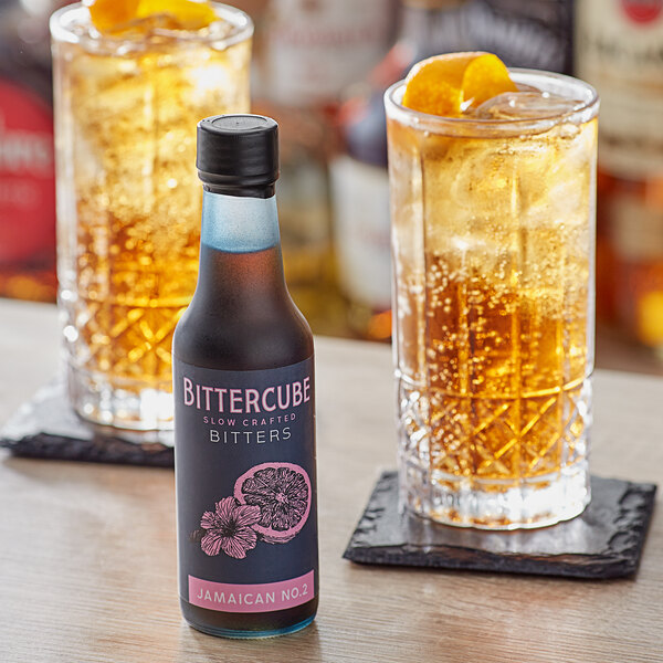 A close-up of a bottle of Bittercube Jamaican No. 2 Bitters next to a glass of liquid.