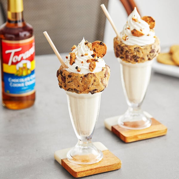 Two glasses of ice cream with cookies and Torani Chocolate Chip Cookie Dough flavoring syrup on a table.