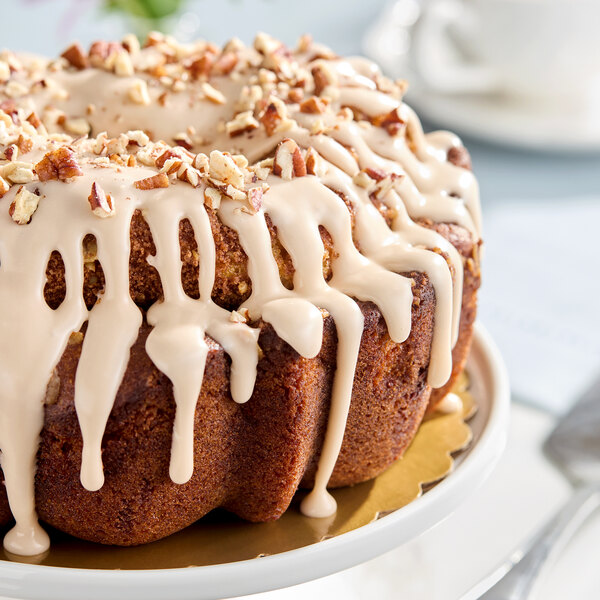 A bundt cake topped with white icing and chopped nuts, displayed on a cake stand.