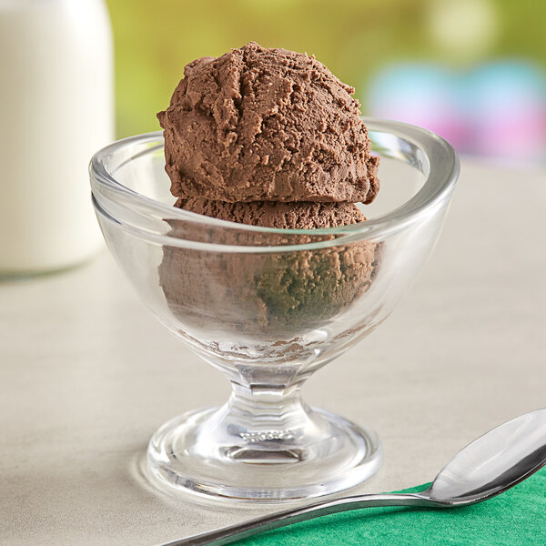 A glass bowl of chocolate ice cream with a spoon.