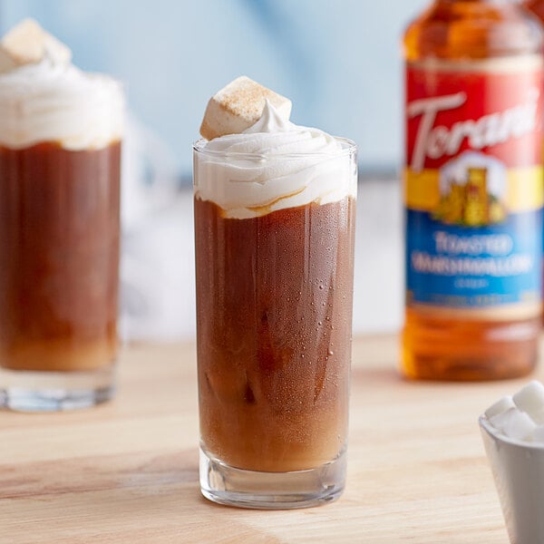 A glass of brown liquid with ice and marshmallows on top.