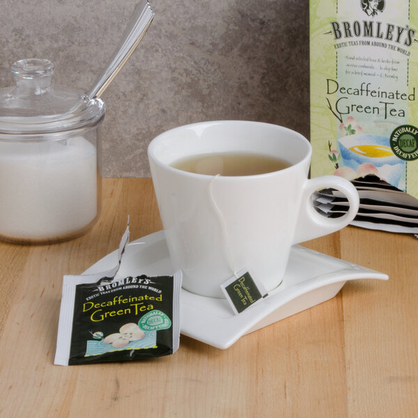 A cup of decaffeinated green tea on a saucer with a Bromley Exotic Green Decaffeinated Tea box on a table.