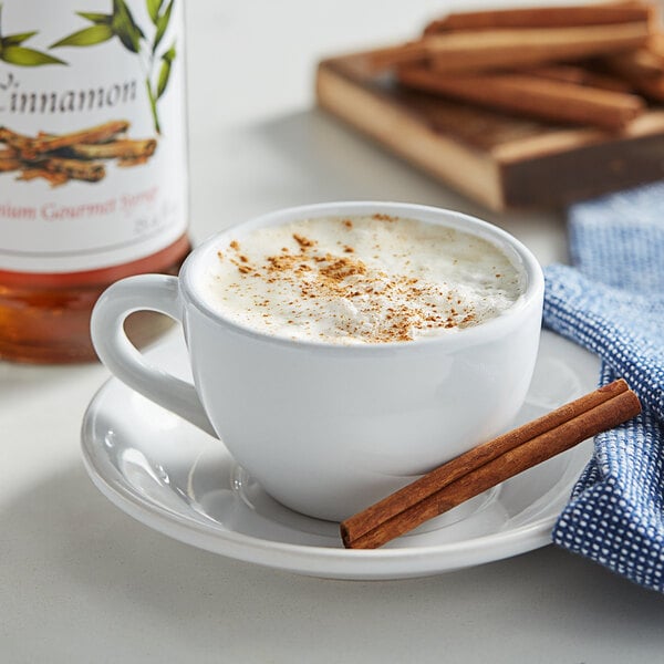 A cup of coffee with cinnamon sticks and a bottle of Monin Cinnamon Flavoring Syrup.