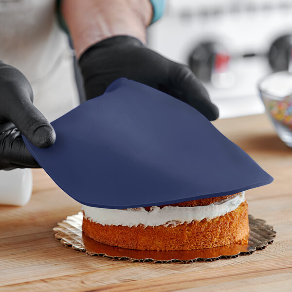 A person wearing black gloves using a knife to cut a Navy blue cake decorated with Satin Ice fondant.