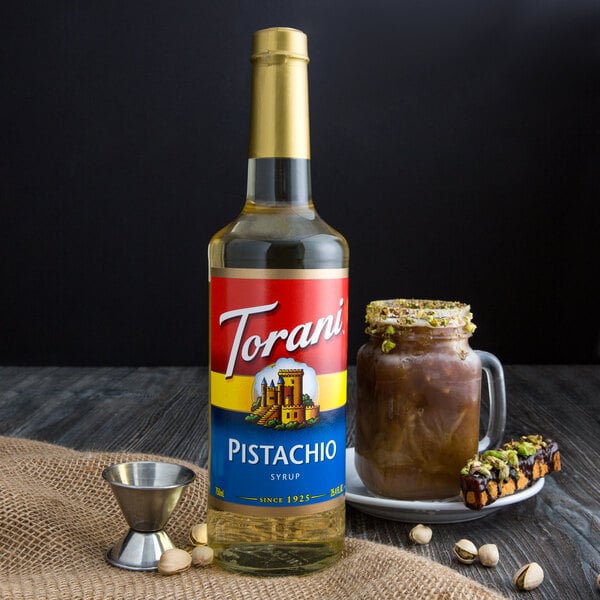 A close up of a Torani Pistachio flavoring syrup bottle on a table with a cup of brown liquid.