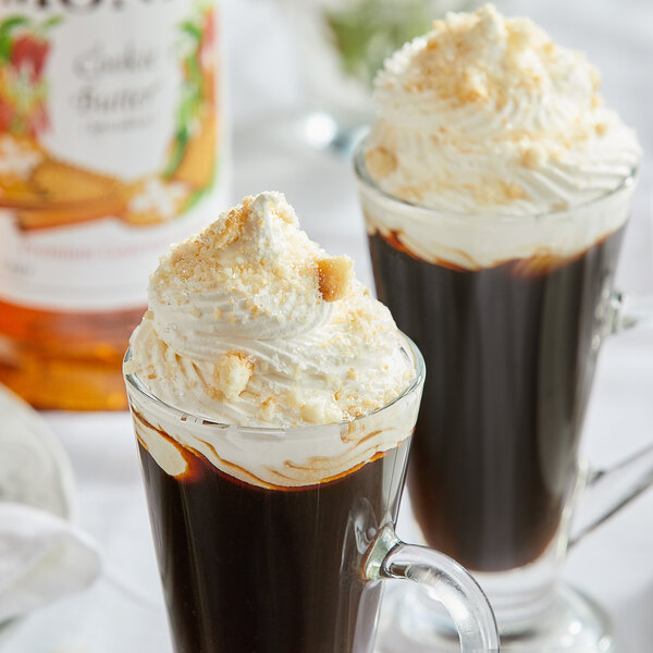 A glass cup of coffee with whipped cream and brown Monin Cookie Butter syrup.